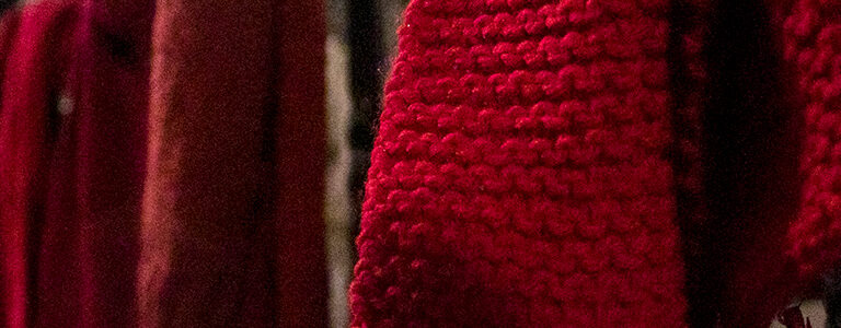 Red knitted scarfs hanging on a metal fence.