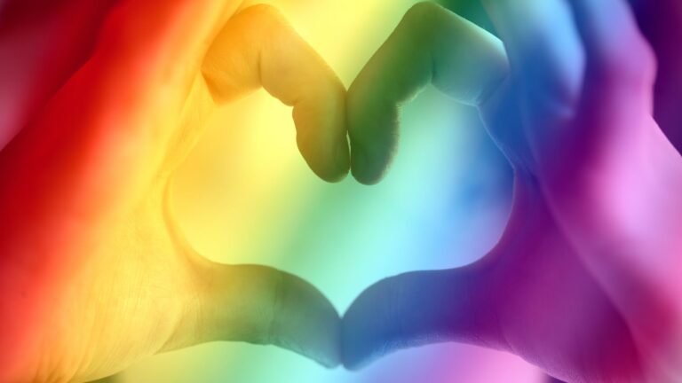 A pair of hands making a heart with a rainbow coloured overlay.