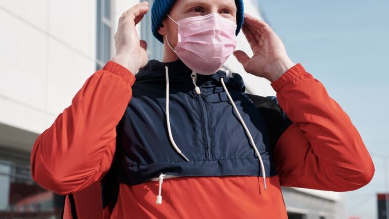 A man on a scooter puts on a pink medical mask.