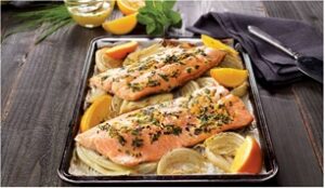 A tray of cooked orange trout topped with slices of lemon and herbs.