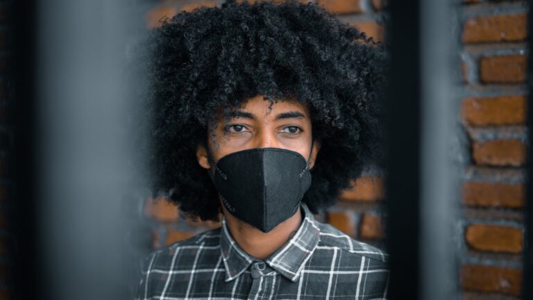 A man wearing a black medical mask looks into the distance behind blurred posts.