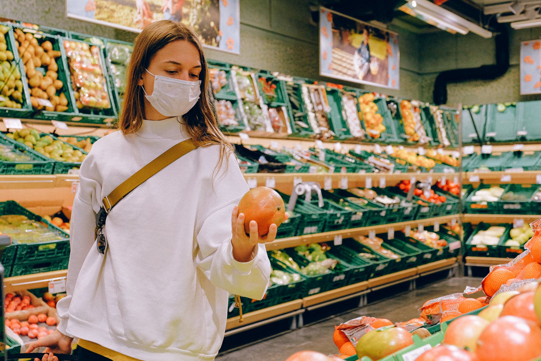 A woman wearing a medical mask examines an orange in a grocery store isle.