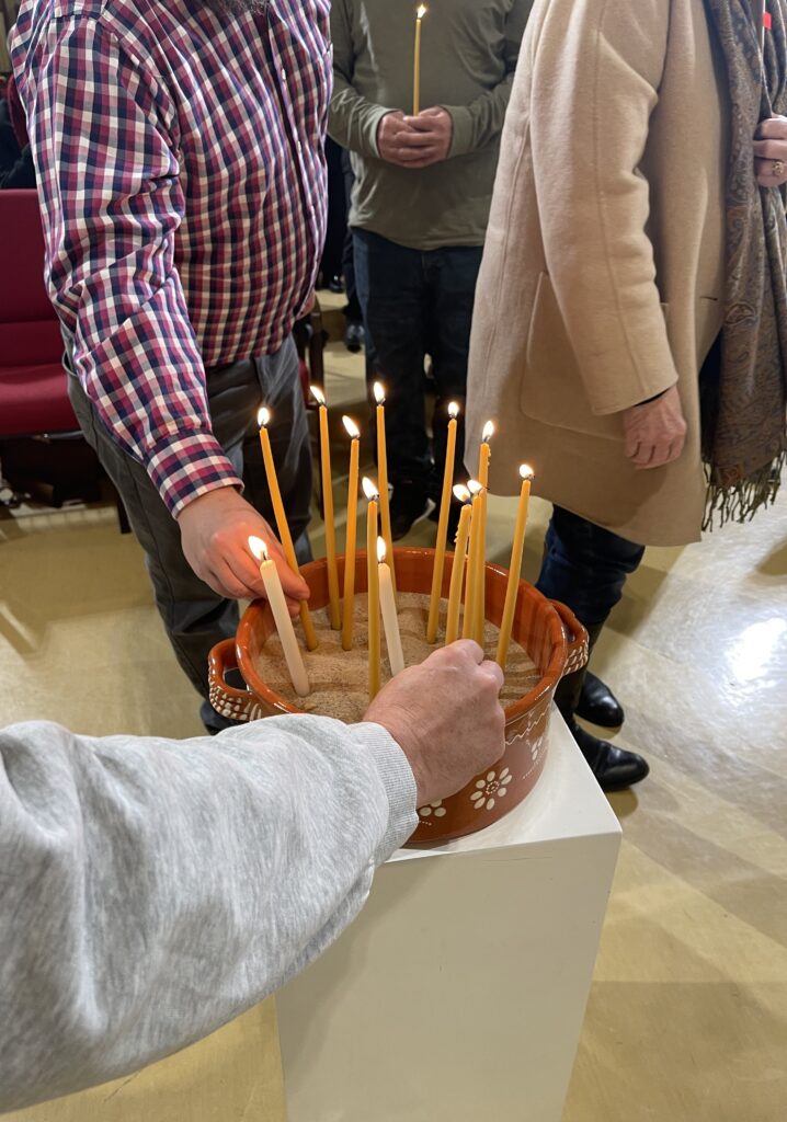 Two hands reaching forward to place candles into a pot on a pedestal.