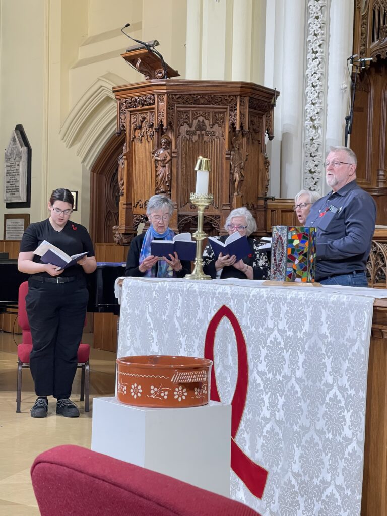 A choir sings in a church behind an alter with an AIDS Network embroidered cover.