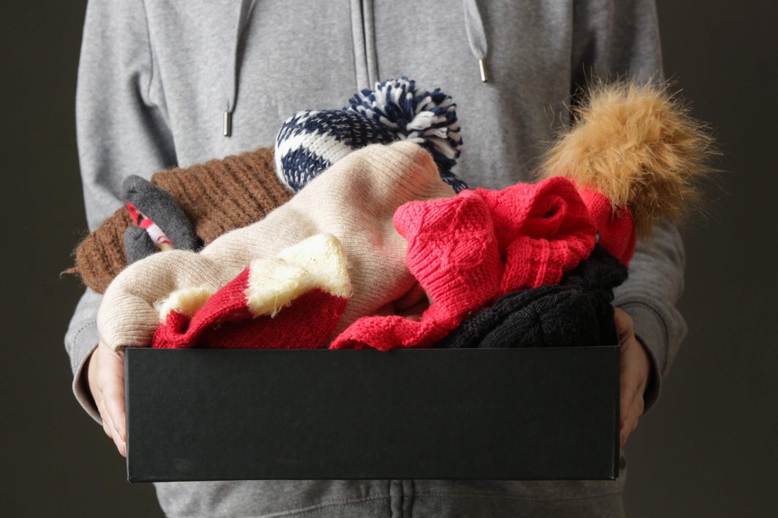 A variety of winter clothes in a box being held.